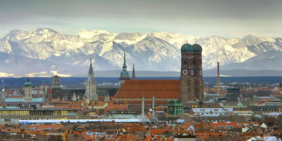 Die Frauenkirche in München steht vor den schneebedeckten Alpen.