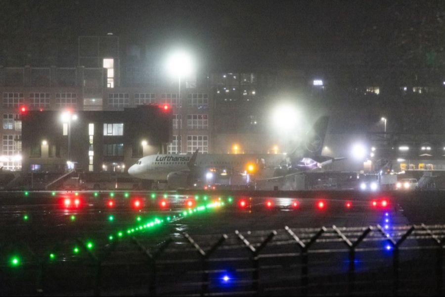 Ein Flugzeug der Lufthansa steht bei Dunkelheit und Schneefall auf dem Flughafen. Aufgrund der Wetterlage mussten am Vortag zahlreiche Flüge gestrichen werden.
