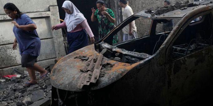 Menschen gehen an einem Auto vorbei, das beim Brand in einem Treibstoffdepot zerstört wurde. Menschen gehen an einem Auto vorbei, das beim Brand in einem Treibstoffdepot zerstört wurde.