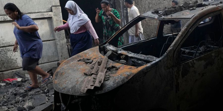 Menschen gehen an einem Auto vorbei, das beim Brand in einem Treibstoffdepot zerstört wurde.