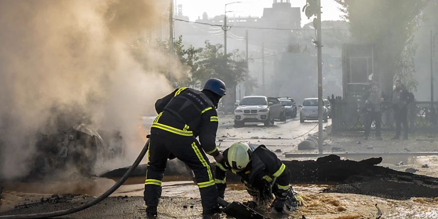 Ein Feuerwehrmann hilft seinem Kollegen aus einem mit Wasser gefüllten Krater, während sie ein brennendes Auto löschen. Nach russischen Raketenangriffen ist der Luftalarm in der ukrainischen Hauptstadt Kiew nach mehr als fünfeinhalb Stunden aufgehoben worden. Foto: Roman Hrytsyna/AP/dpa