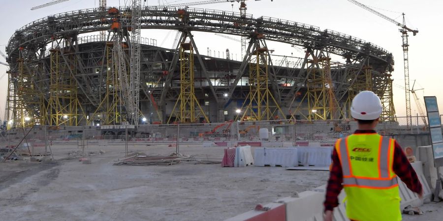 Ein Mann mit Schutzhelm und Schutzweste geht über die Baustelle des Lusail Iconic Stadiums.