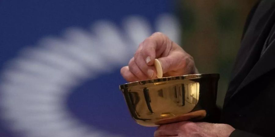 Ein Mitglied der Kirchengemeinde hält während eines Gottesdienstes mit Abendmahl im katholischen Dom St. Bartholomäus vor dem Logo des ÖKT eine Oblate in der Hand. Foto: Sebastian Gollnow/dpa