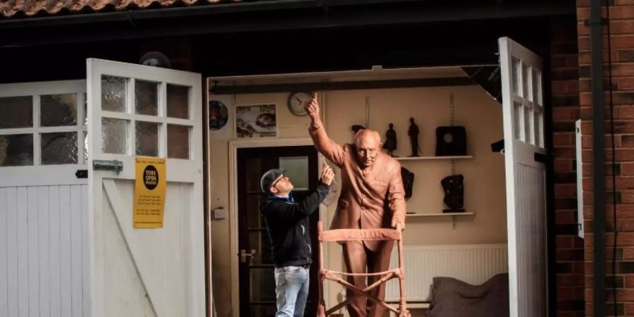 Andrian Melka legt den letzten Schliff an eine zwei Meter hohe Tonstatue von Kapitän Sir Tom Moore in seinem Studio. Foto: Danny Lawson/PA Wire/dpa