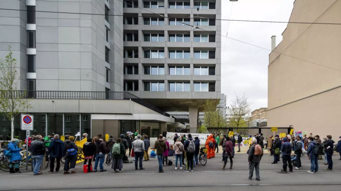 Demonstrierende in Basel vor dem Gebäude von Bayer & Syngenta, 17. April 2021. Im Hintergrund ist ein Werbeplakat für die Trinkwasser-Initiative sichtbar. Bayer Syngenta Demonstration