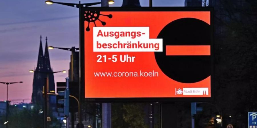 Eine Anzeigetafel in Köln weist Ende April auf die Ausgangsbeschränkung zwischen 21:00 und 05:00 Uhr hin. Foto: Oliver Berg/dpa