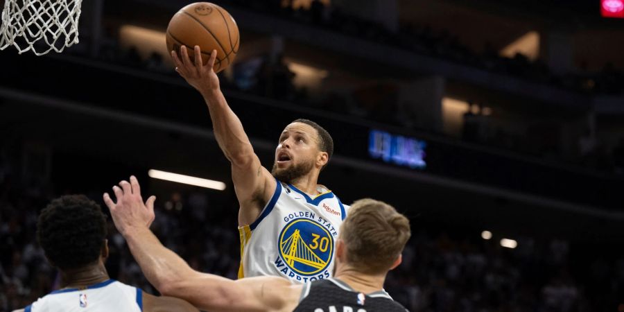 Stephen Curry von den Golden State Warriors in Aktion mit Teamkollege Andrew Wiggins (l) und Domantas Sabonis von den Sacramento Kings.