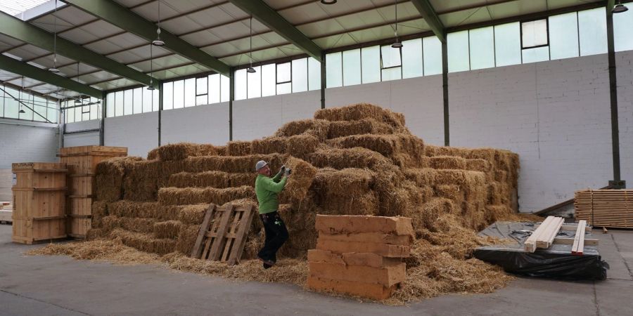 Ein Handwerker holt einen Strohballen als Dämmung für Bauteile eines Gebäudes. In Michelstadt entsteht ein Büro- und Betriebsgebäude aus Holz und Stroh.