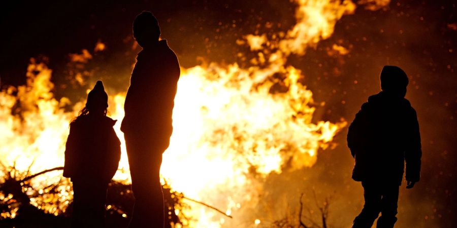 Ein Mann und zwei Kinder stehen vor einem Osterfeuer.