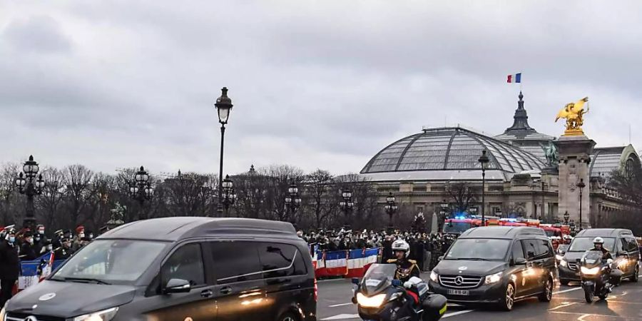 Fahrzeuge mit den Särgen von drei französischen Soldaten fahren in Paris über die Brücke Alexandre III an einer Gruppe von Menschen vorbei, die den Soldaten gedenken. Foto: Alain Jocard/AFP/dpa