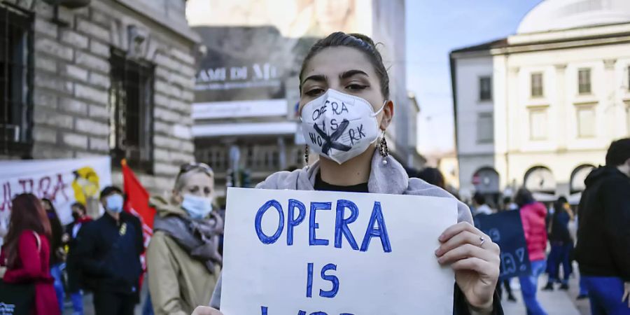 Eine Frau mit Mundschutz hält bei einer Demonstration gegen die Massnahmen der Regierung zur Eindämmung der Corona-Pandemie ein Schild mit der Aufschrift «Opera is work» (zu deutsch: «Oper ist Arbeit») in den Händen. Foto: Claudio Furlan/LaPresse/AP/dpa