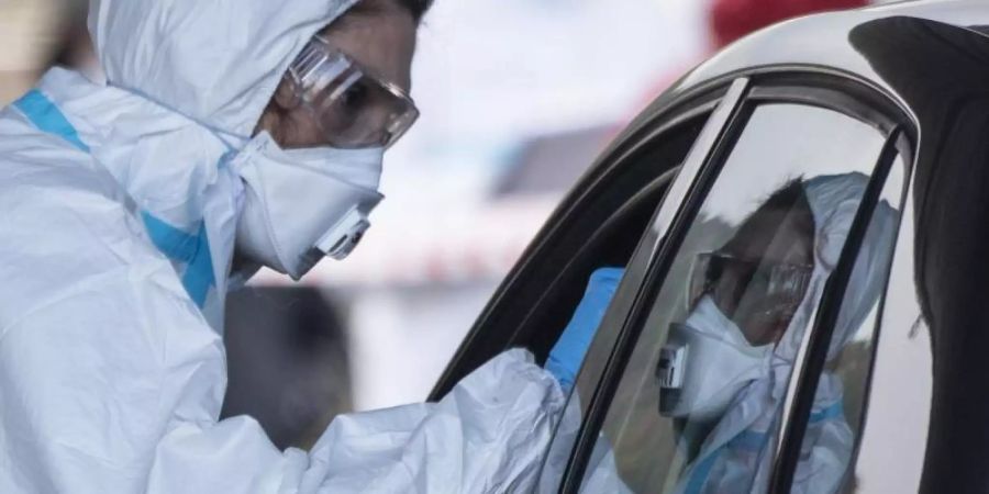 Ein Mitarbeiter eines Corona-Testzentrums auf dem Marburger Messegelände nimmt einen Abstrich von einem Autofahrer. Foto: Boris Roessler/dpa