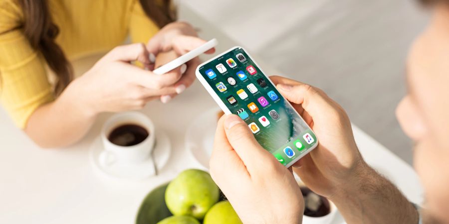 Zwei Personen sitzen sich bei einem Kaffee gegenüber und schauen parallel auf ihre Smartphones.