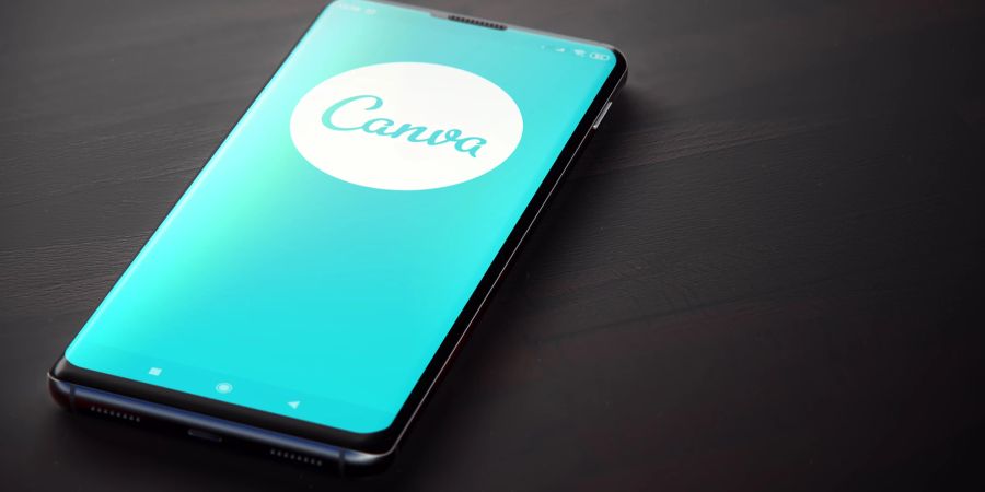 Auf einem Tisch liegt ein Smartphone, das die Canva App zeigt.