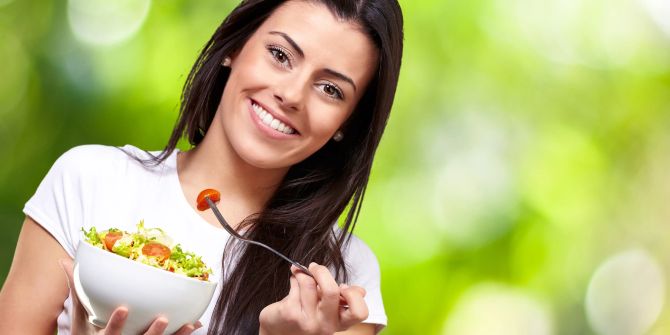 Frau mit langen Haaren isst Salat.