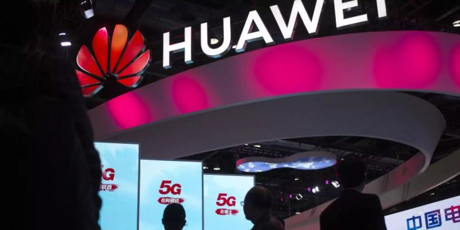 Besucher gehen an einem Display für 5G-Dienste des chinesischen Technologieunternehmens Huawei auf der PT Expo in Peking vorbei. Foto: Mark Schiefelbein/AP/dpa