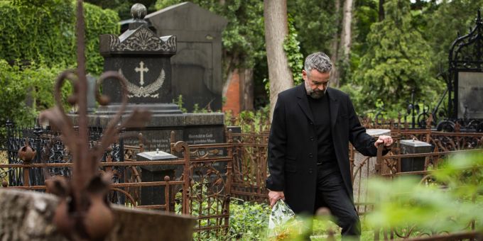 Bei der Trauerbewältigung können auch Rituale helfen, neben dem Schwelgen in Erinnerungen und das Anzünden von Kerzen auch der Gang zum Grab des Verstorbenen. Mann Friedhof schwarz Grabsteine