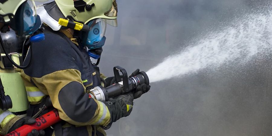 Ein Feuerwehrmann bekämpft einen Brand mit einem Wasserschlauch. (Archivbild)