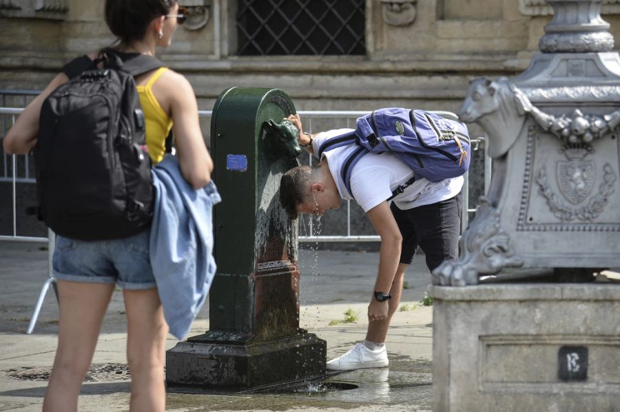 Ein Mann kühlt sich an einem Trinkbrunnen ab.