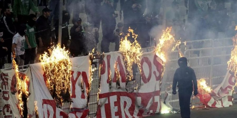 Vermummte Fans verbrennen während des Derbys ein Banner vor den Zuschauertribünen. Foto: InTime Sports via AP