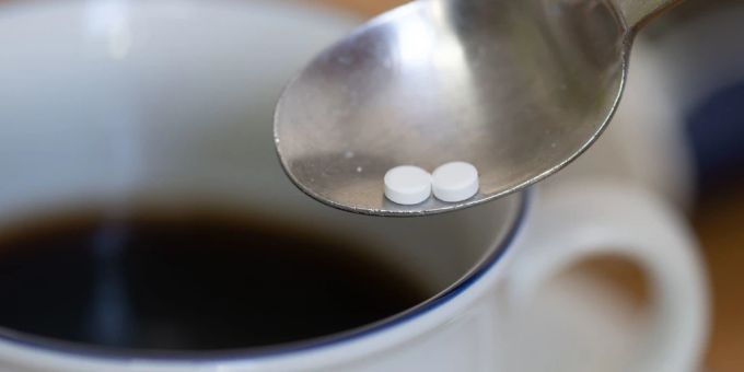 Ein Löffel mit zwei Süssstofftabletten ist über einer Tasse Kaffee zu sehen. Süssstoff, Kaffee