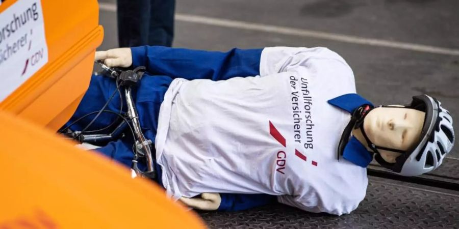 Bei einem Crashtest der Unfallforscher der Versicherer liegt ein Crashtest-Dummy mit seinem Fahrrad auf der Strasse, nachdem er gegen eine geöffnete Tür eines geparkten Autos fuhr - einem sogenannten Dooring-Unfall. Foto: Guido Kirchner/dpa