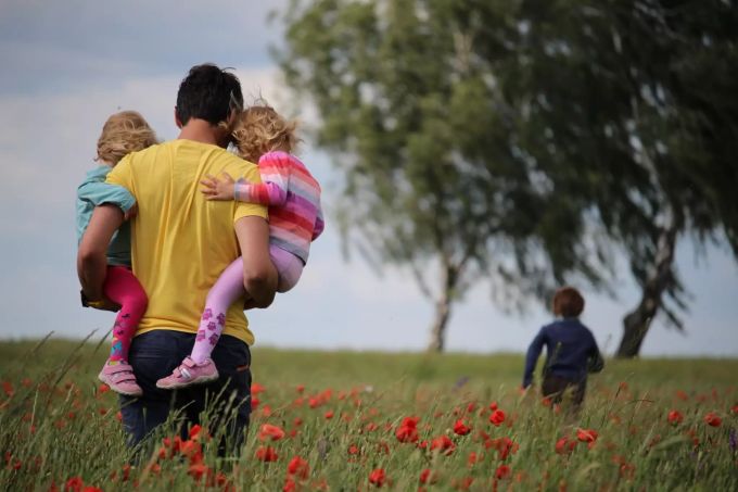 Helikopter-Eltern blockieren ihre Kinder in der Selbständigkeit. Vater mit zwei Kinder auf dem Arm.
