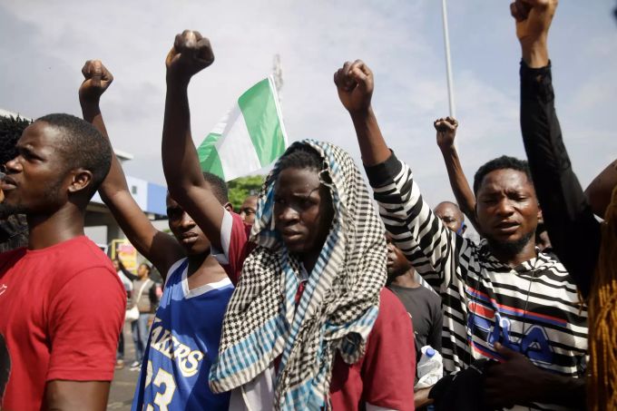 Teilnehmer einer Demonstration gegen Polizeigewalt in Lagos strecken ihre geballte Fäuste in die Höhe und einer der Demonstranten hält eine Fahne Nigerias. Proteste in Nigeria