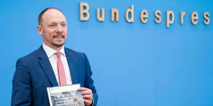 Marco Wanderwitz (CDU), Ostbeauftragter der Bundesregierung, zeigt bei der Vorstellung den Jahresbericht zum Stand der Deutschen Einheit 2020. Foto: Christophe Gateau/dpa
