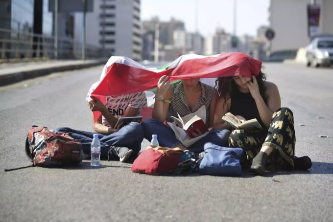 Drei Frauen protestieren gegen die Regierung, indem sie auf der Strasse sitzend Bücher lesen und den Verkehr blockieren. libanon