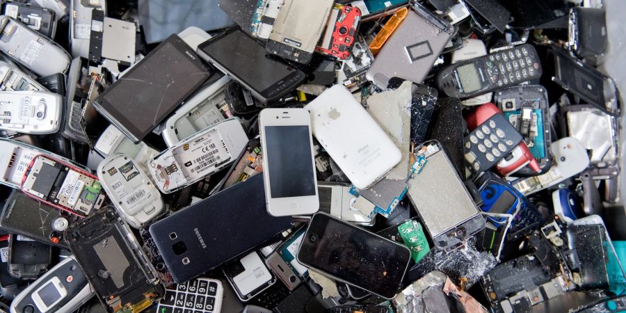 Alte Handys und Smartphones liegen in einem Container, ehe sie geschreddert werden.