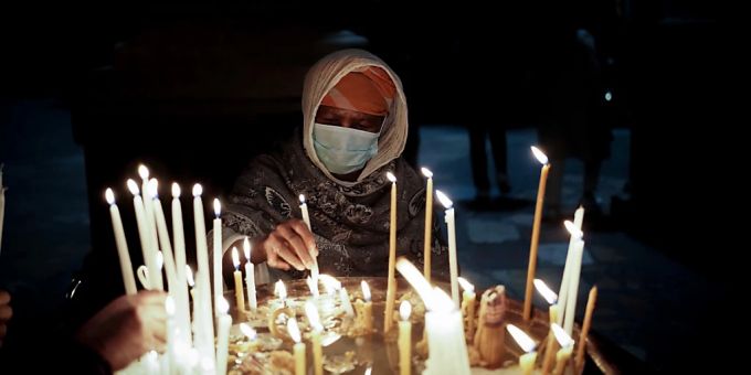Eine Frau mit Mund-Nasen-Schutz zündet Kerzen an und betet an Heiligabend in der Grabeskirche in Jerusalem. Jerusalem