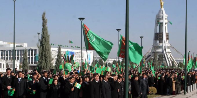 Menschen begrüssen den neuen Präsidenten in Ashgabat mit dem Neutralitätsbogen im Hintergrund Menschen in Anzügen und mit Flaggen