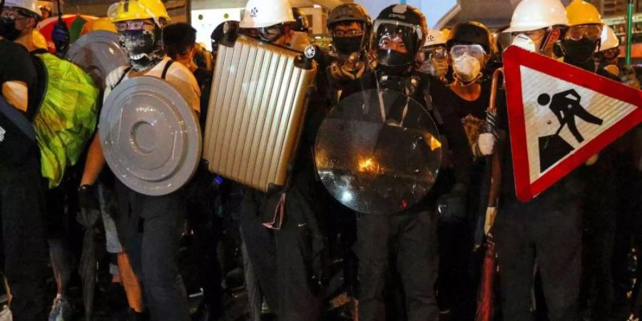 Demonstranten haben sich mit Strassenschildern, Koffern und Mülleimerdeckeln gegen die Schlagstöcke der Polizisten gewappnet. Foto: Bobby Yip/AP