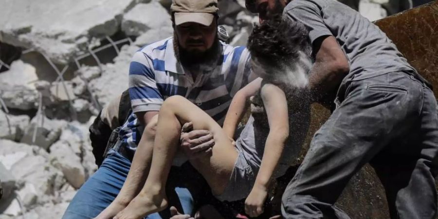 Mitglieder der syrischen Weisshelme und Freiwillige retten ein verletztes Kind aus den Trümmern eines Gebäudes, das bei einem Luftangriff durch die syrischen Regierungskräfte beschädigt wurde. Foto: Anas Alkharboutli