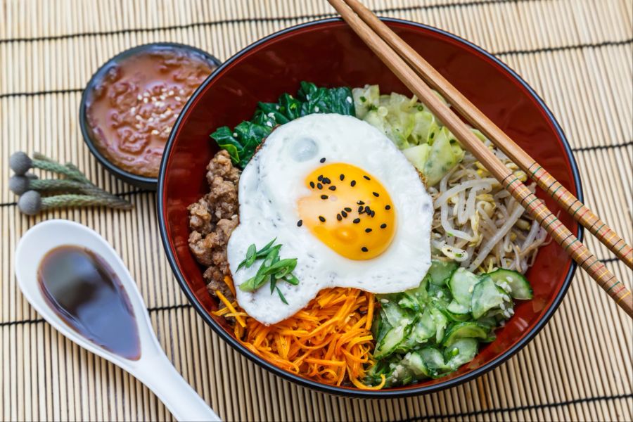 Bibimbap in einer Schüssel auf Bambusmatte.