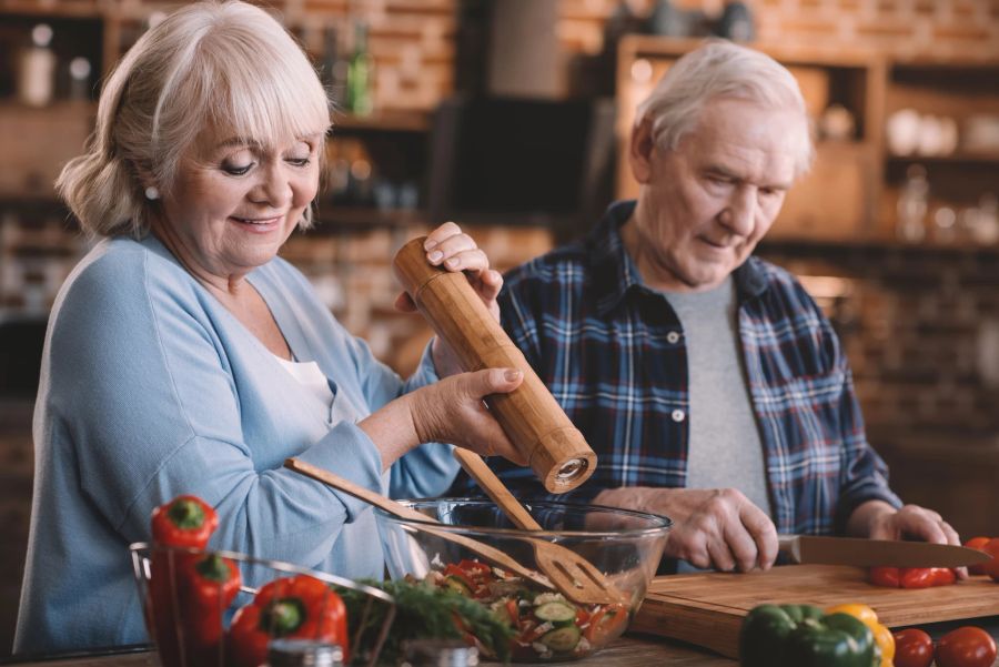 altes paar beim kochen, salat zubereiten