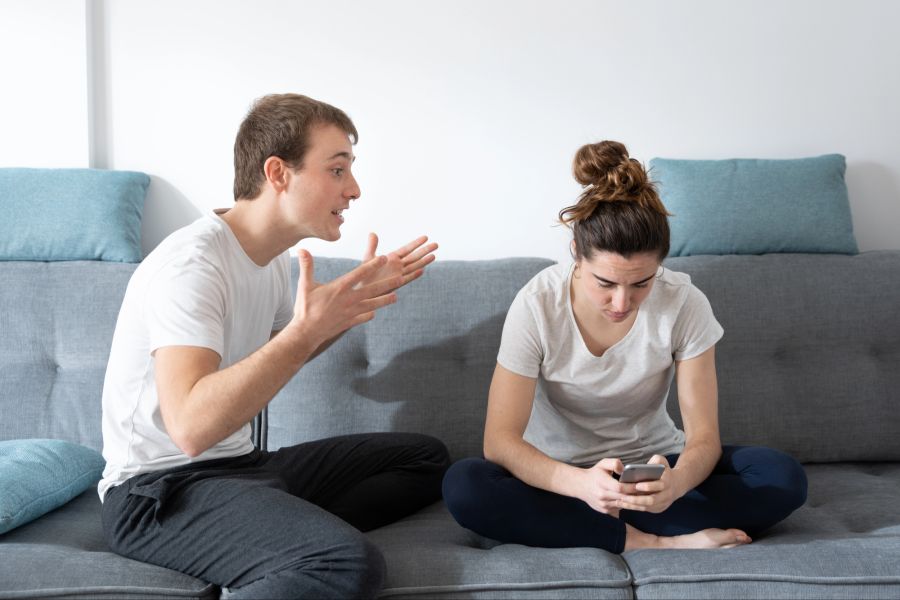 Junger Mann spricht energisch mit Frau, die auf ihr Smartphone guckt