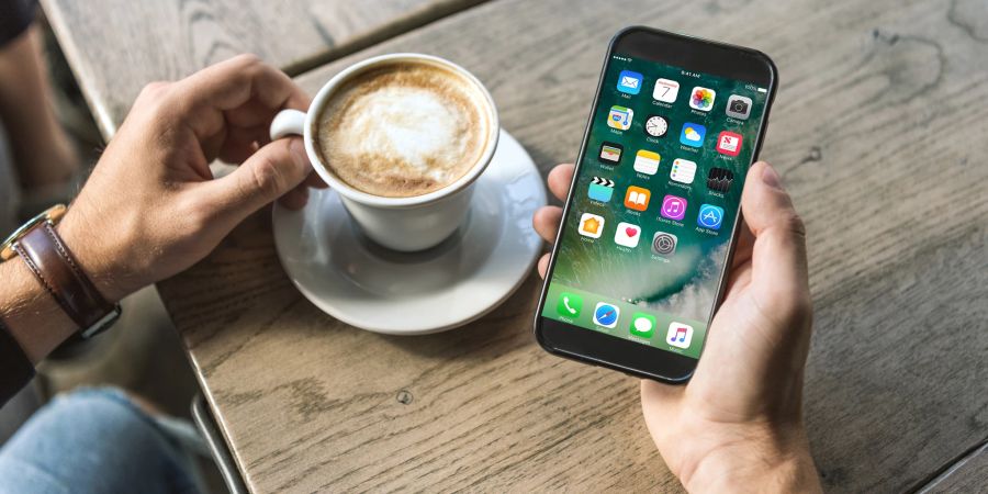 Handy-Nutzer blickt auf sein Smartphone und trinkt Cappuccino