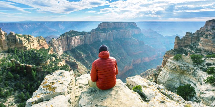 Mann mit roter Jacke sitzt im Grand Canyon