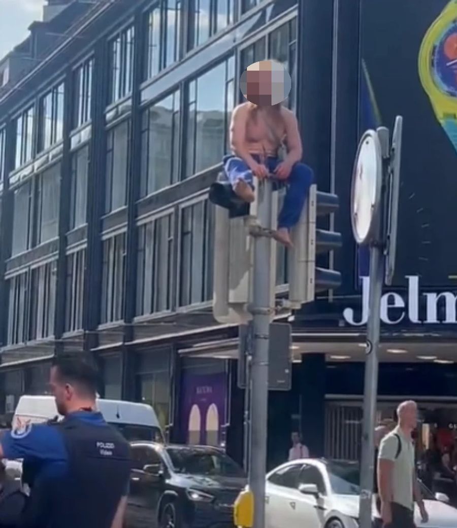 Ein Beispiel: Ein Mann mit langen Haaren, der in Zürich oben ohne und mit nackten Füssen auf einer Ampel sitzt. Nau.ch hat sein Gesicht verpixelt.