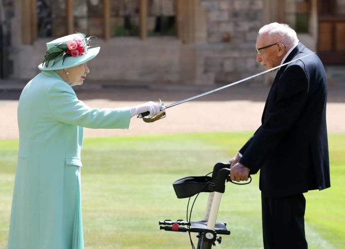 ARCHIV - 17.07.2020, Grossbritannien, Windsor: Königin Elizabeth II. (l) schlägt Sir Tom Moore (r), Weltkriegsveteran und Rekord-Spendensammler, während einer Zeremonie im Freien auf Schloss Windsor zum Ritter. Captain Tom nach Corona-Infektion gestorben
