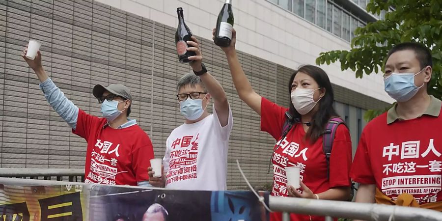 Pro-Chinesische Aktivisten feiern das Urteil mit Champagner. Ein Hongkonger Gericht verkündete das Strafmass gegen neun bekannte demokratische Aktivisten und Politiker wegen illegaler Versammlung 2019. Foto: Vincent Yu/AP/dpa