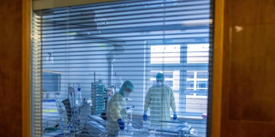 Mediziner und Pfleger versorgen einen an Covid-19 erkrankten Patienten in einem Zimmer des besonders geschützten Teils der Intensivstation des Universitätsklinikums Greifswald. Foto: Jens Büttner/dpa-Zentralbild/dpa