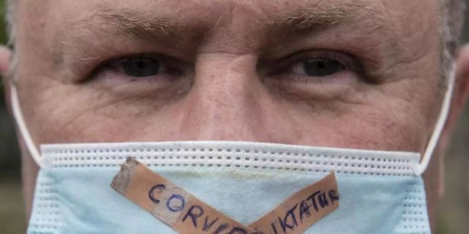 Ein Teilnehmer einer Kundgebung gegen die Corona-Massnahmen der Regierung trägt einen Mundschutz mit der Aufschrift "Merkel-Diktatur - Covid-Fake". Foto: Boris Roessler/dpa Ein Teilnehmer einer Kundgebung gegen die Corona-Massnahmen der Regierung trägt einen Mundschutz mit der Aufschrift "Merkel-Diktatur - Covid-Fake". Foto: Boris Roessler/dpa