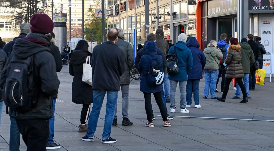 Zahlreiche Menschen stehen auf dem Alexanderplatz vor einem Elektronik-Fachmarkt.