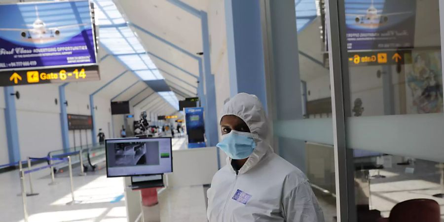 Ein Flughafenmitarbeiter im Schutzanzug und mit Mund-Nasen-Bedeckung steht neben einem Temperaturscanner in einem Terminal am Katunayake International Airport. Foto: Eranga Jayawardena/AP/dpa