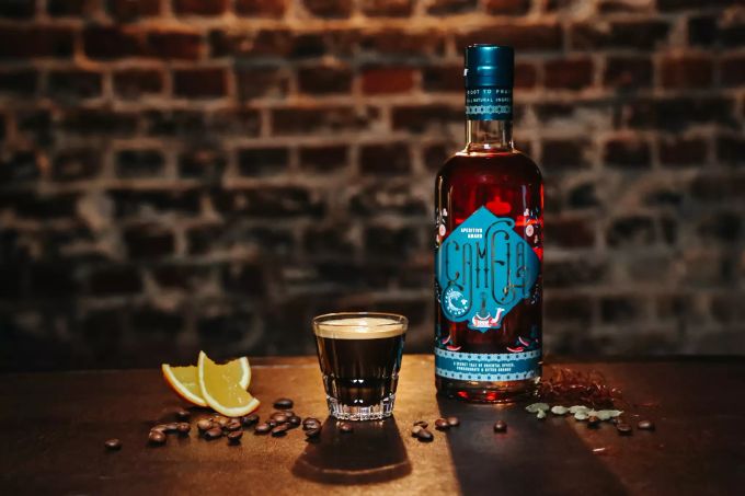 Für einen «Camela Coffee Shot» werden einfach in einen frischen Espresso 20 ml Camela, ein herber Aperitif mit orientalischen Gewürzen, eingerührt. Flasche Camela blaues Etikett Shot Caffe zwei Orangenschnitze