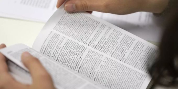 Eine Person schlägt ein Wort im Wörterbuch nach. (Symbolbild) Wörterbuch
