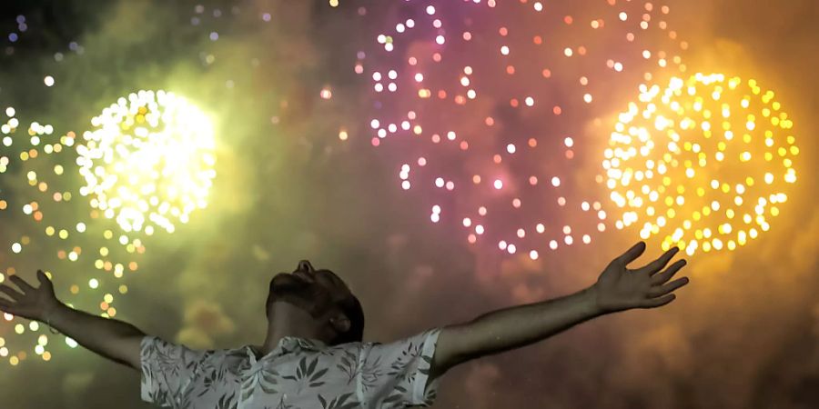 dpatopbilder - Ein Mann feiert den Beginn des neuen Jahres, während im Hintergrund ein Feuerwerk über dem Copacabana-Strand in Rio De Janeiro den Nachthimmel erleuchtet. Foto: Bruna Prado/AP/dpa